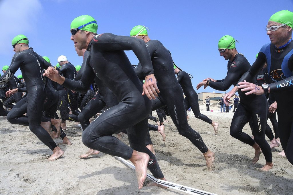 Pływacy w piankach do triathlonu wbiegają do wody z plaży