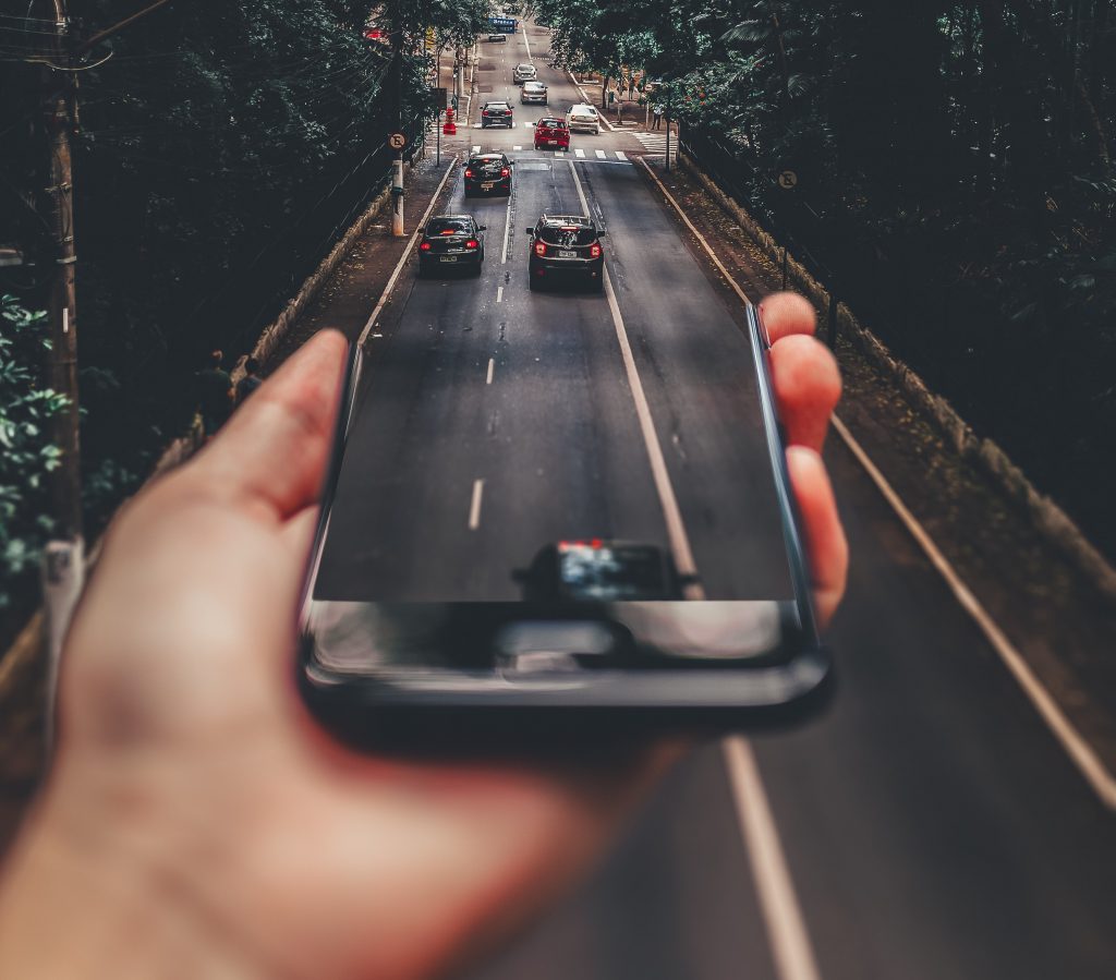 Grafika - telefon komórkowy zlewający się z drogą, na której poruszają się samochody