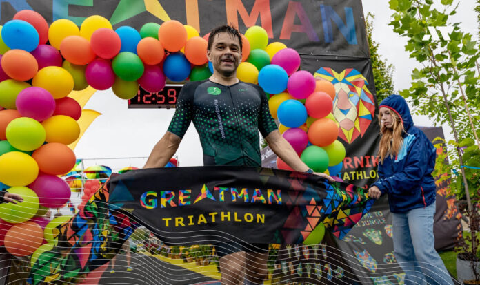 Zawodnik na mecie Greatman Triathlon 2025 trzymający flagę wydarzenia