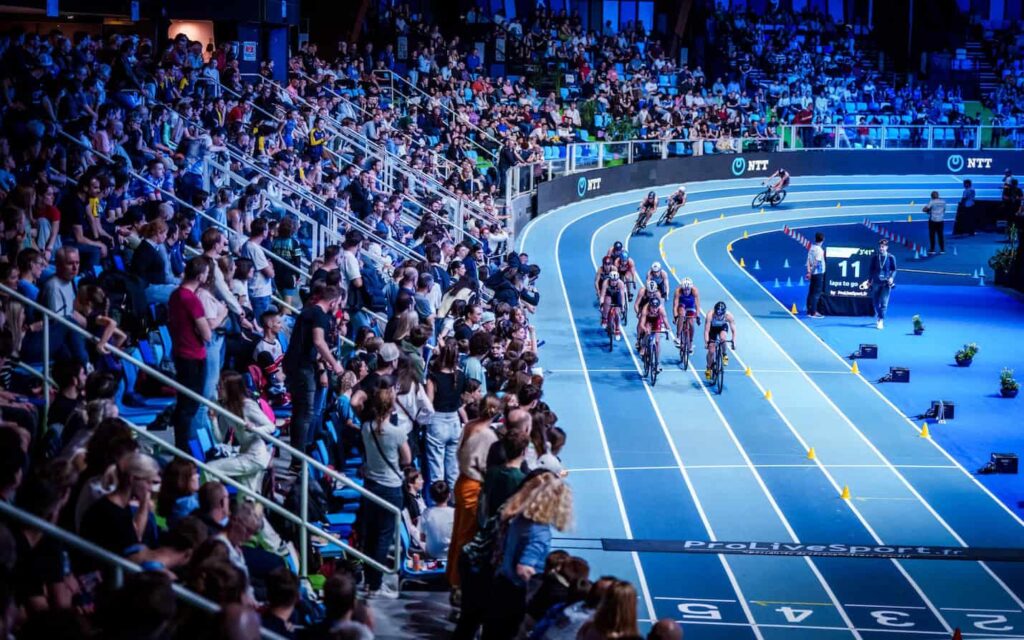Zawodnicy rywalizujący podczas T1 Liévin World Triathlon Indoor Cup na hali lekkoatletycznej, przy pełnych trybunach kibiców