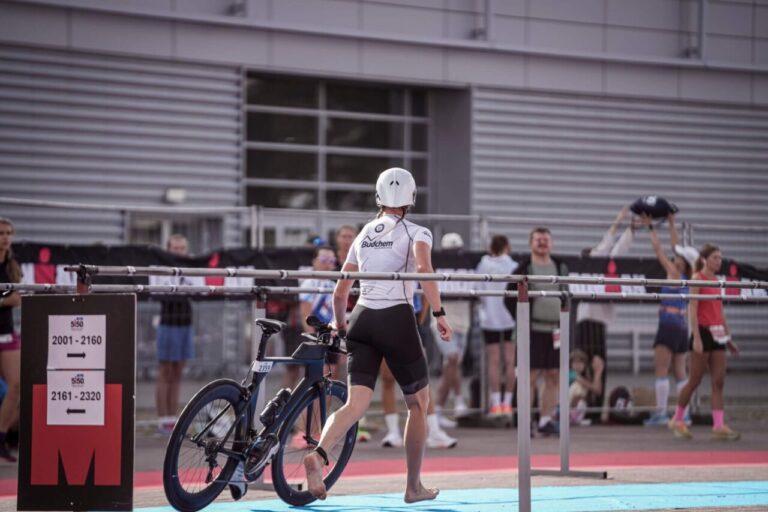 Zawodniczka prowadząca rower w strefie zmian T1 podczas triathlonu – organizacja i logistyka debiutu.