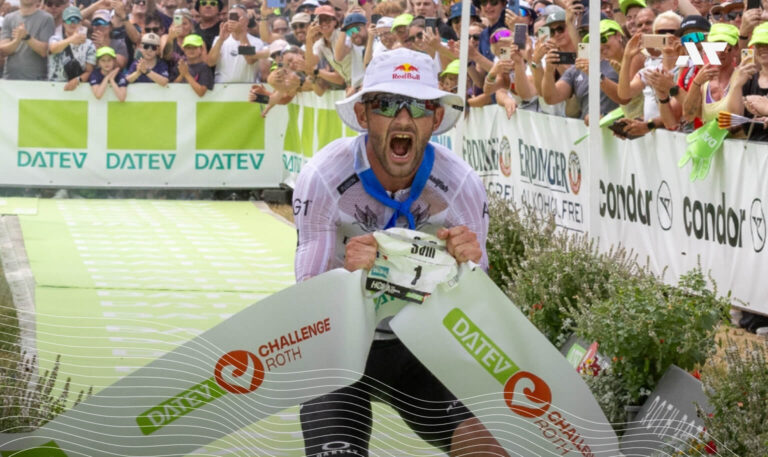 Zawodnik przekracza linię mety podczas DATEV Challenge Roth wśród kibiców, trzymając taśmę finiszową.