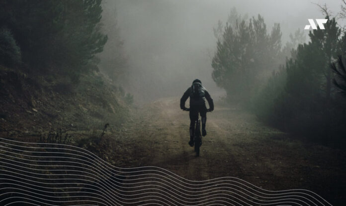 Kolarz na rowerze gravelowym jadący leśną, szutrową drogą we mgle – trening w terenie przed sezonem triathlonowym.