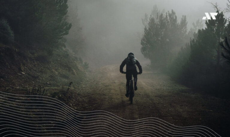 Kolarz na rowerze gravelowym jadący leśną, szutrową drogą we mgle – trening w terenie przed sezonem triathlonowym.