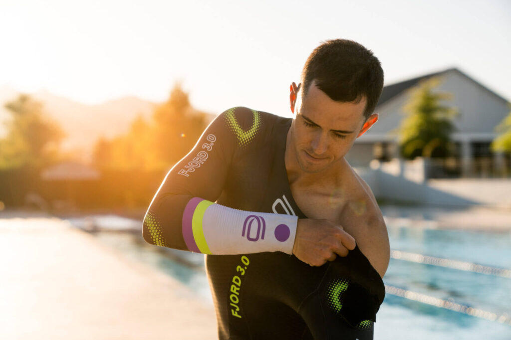 Zawodnik zakładający piankę triathlonową przed pływaniem, przygotowanie do treningu lub startu w wodach otwartych