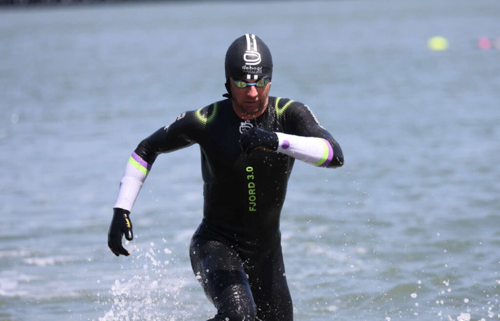 Triathlonista wychodzący z wody w piance triathlonowej podczas pływania w chłodnych warunkach
