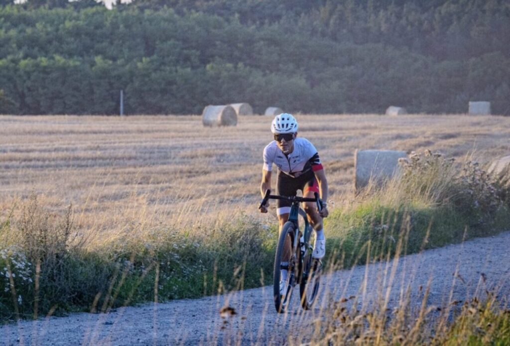 Triathlonista na rowerze gravelowym podczas jazdy po szutrowej drodze – przygotowania do sezonu triathlonowego i budowanie bazy tlenowej.
