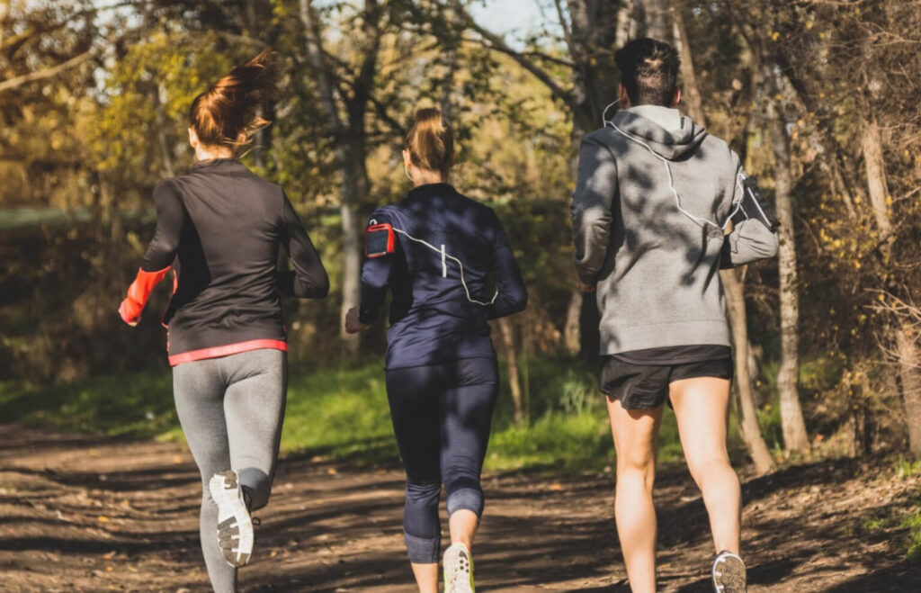 Trzech amatorów biegnących w terenie leśnym podczas lekkiego treningu w okresie taperingu przed startem w triathlonie.